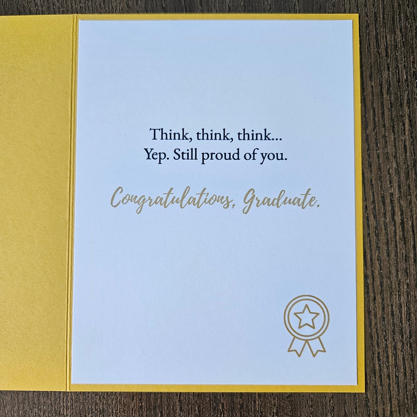 Graduation-themed card with motivational quote and star emblem on a wooden surface