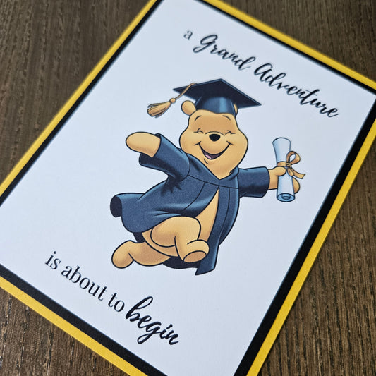 Graduation-themed card with a cartoon bear in a cap and gown on a wooden surface.