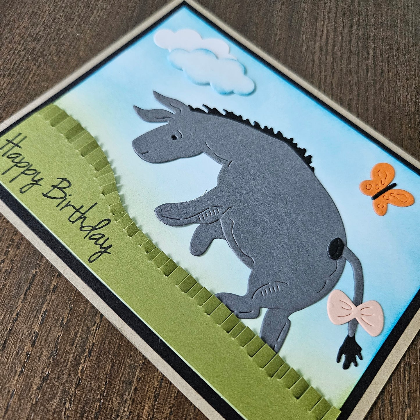 Handmade birthday card with a donkey illustration, butterfly, and 'Happy Birthday' text on a wooden surface.