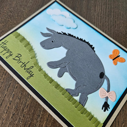 Handmade birthday card with a donkey illustration, butterfly, and 'Happy Birthday' text on a wooden surface.