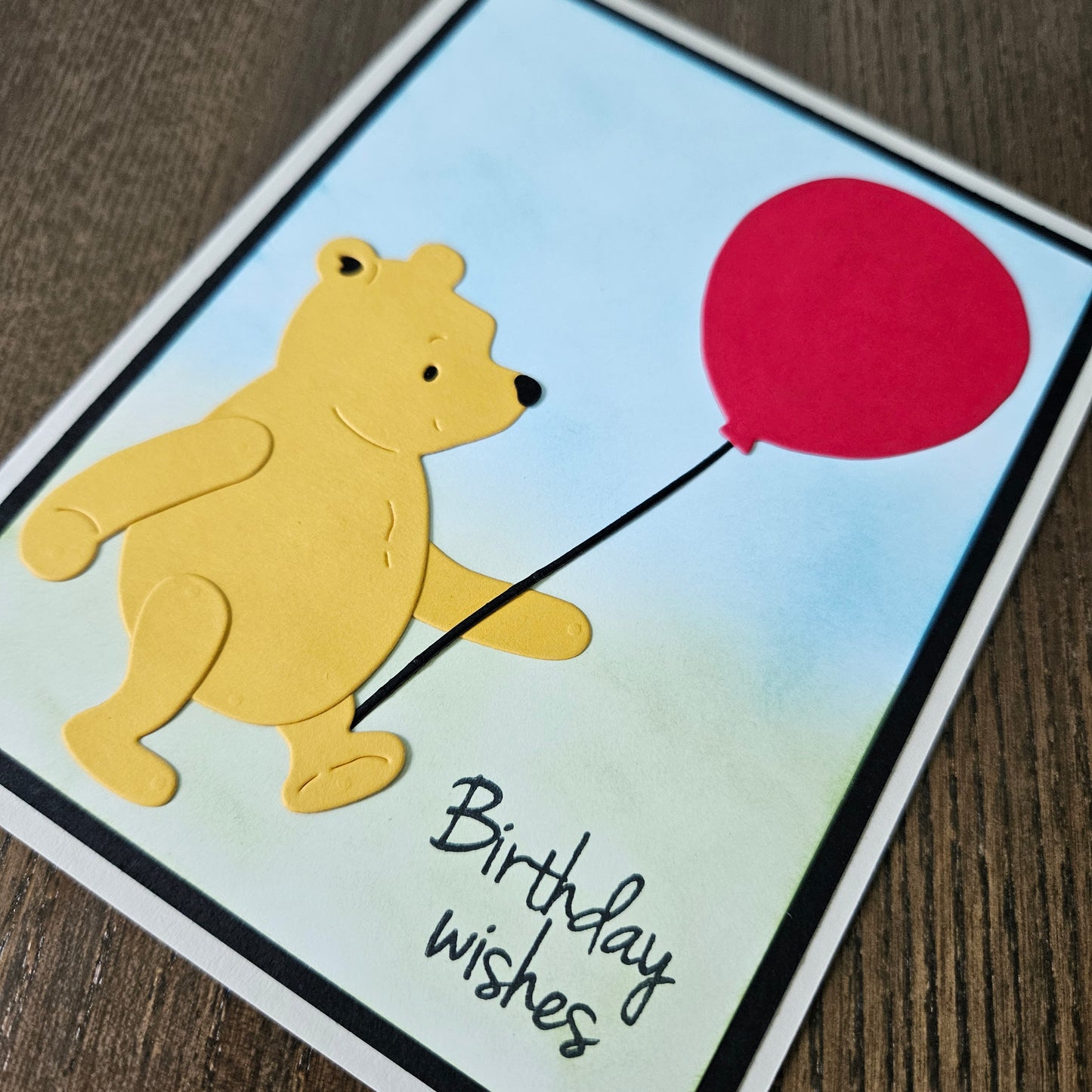 Card with a bear holding a red balloon and 'Birthday wishes' text on a wooden surface