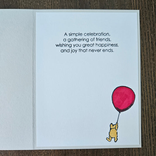 Greeting card with Winnie the Pooh and a red balloon on a wooden surface