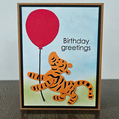 Handmade Winnie the Pooh birthday card featuring a die-cut illustration of Tigger holding a bright red balloon against a soft hand-inked watercolor sky and green meadow background.