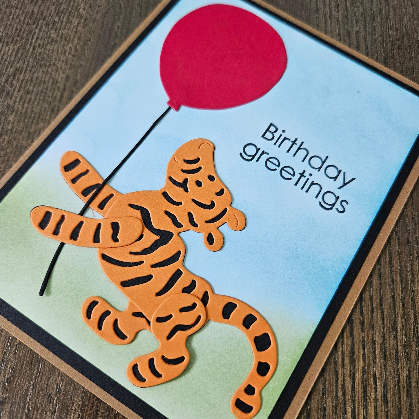 Birthday card with a tiger and red balloon on a wooden surface