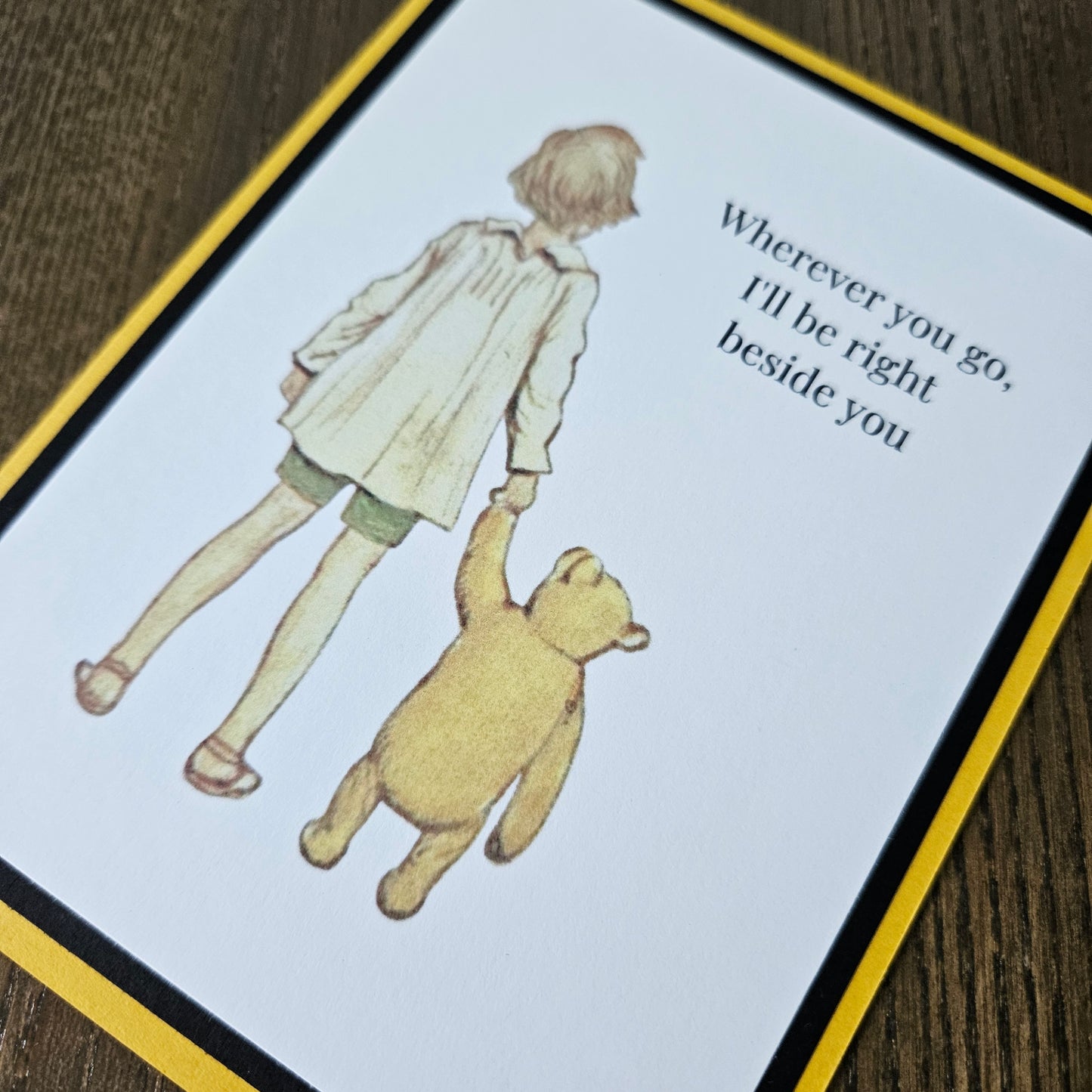 Card with illustration of a child and bear holding hands and text on a wooden surface