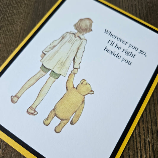 Card with illustration of a child and bear holding hands and text on a wooden surface