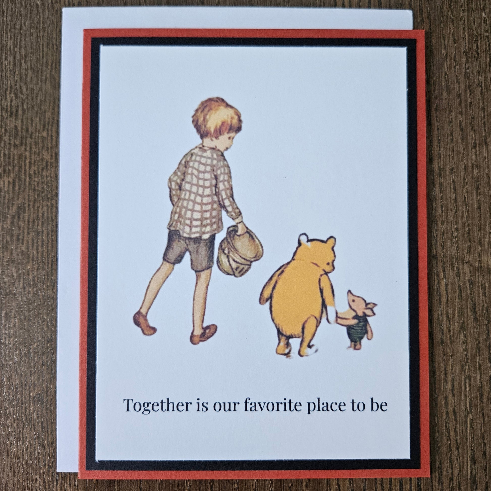 Handmade friendship card featuring a classic illustration of Christopher Robin, Winnie the Pooh, and Piglet walking together, framed by black and rust-red layered cardstock. Text reads Together is our favorite place to be.