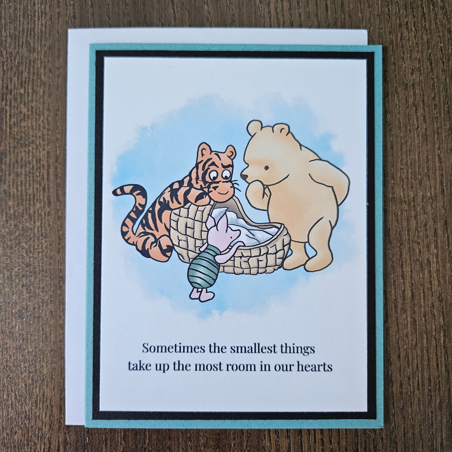 Handmade Winnie the Pooh new baby card featuring a classic watercolor illustration of Pooh, Tigger, and Piglet gathered around a basket, accented by a soft teal layered border.