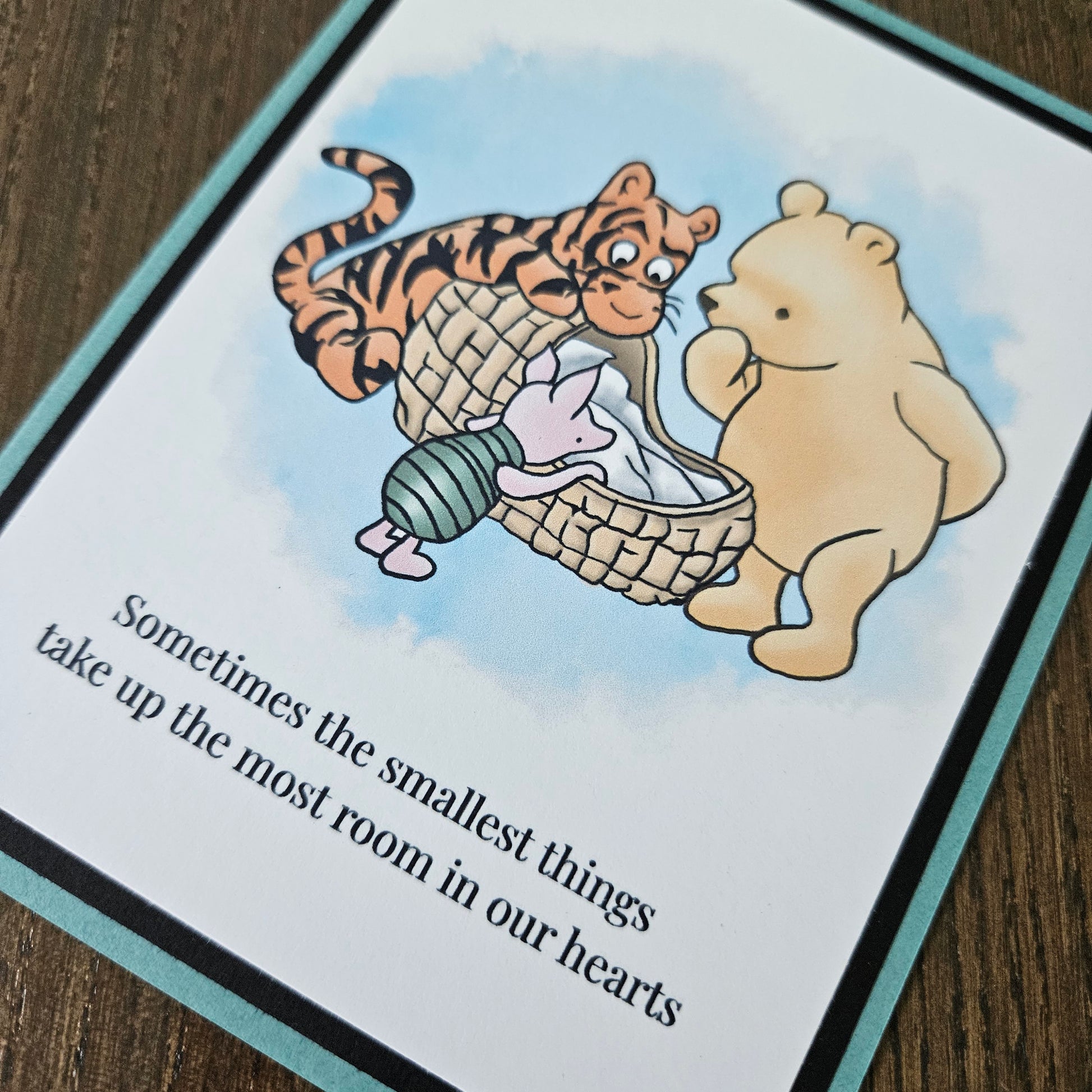Handmade Winnie the Pooh new baby card featuring a classic watercolor illustration of Pooh, Tigger, and Piglet gathered around a basket, accented by a soft teal layered border.