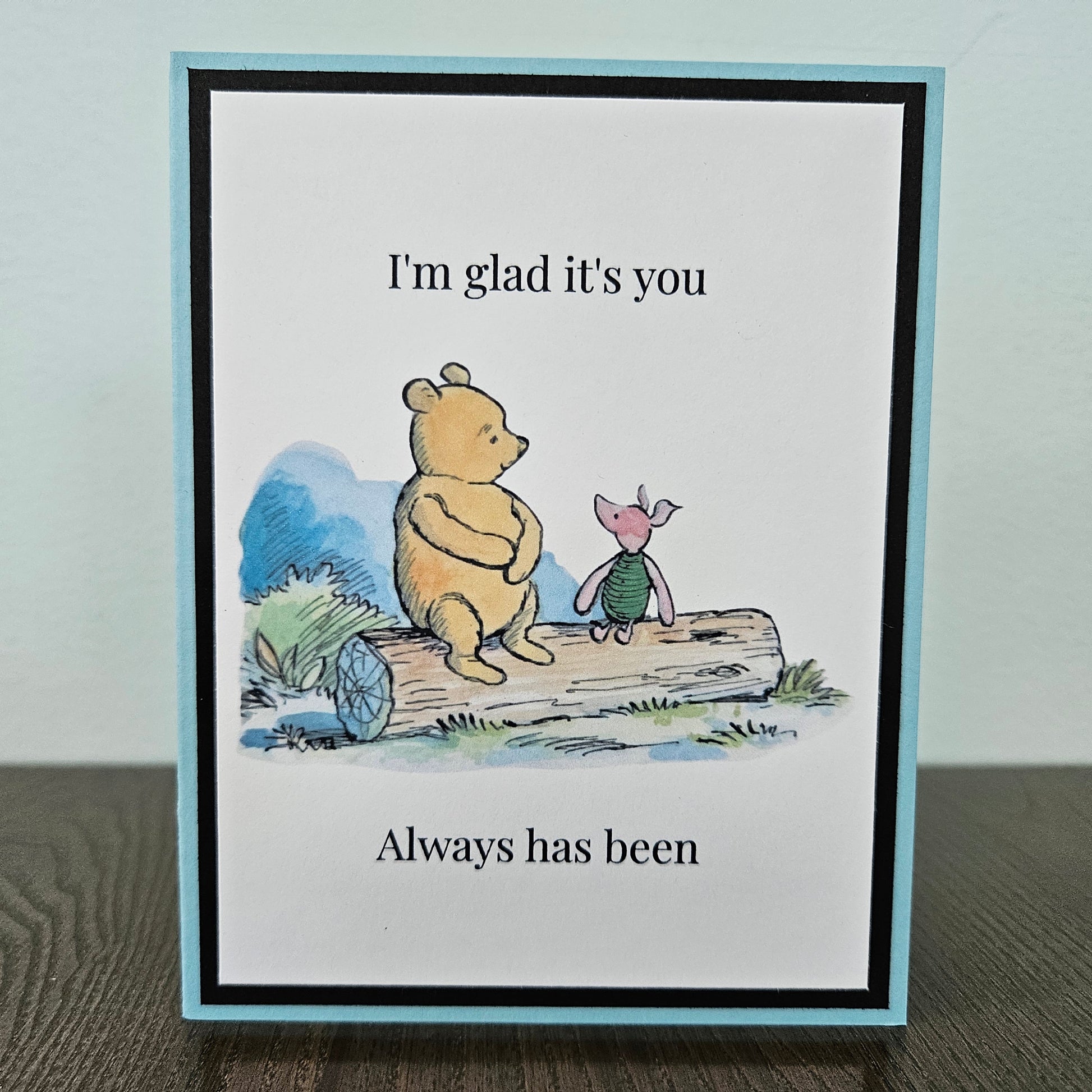 Handmade Winnie the Pooh friendship card featuring a classic watercolor illustration of Pooh and Piglet sitting side by side on a log, accented by a soft sky-blue layered border.