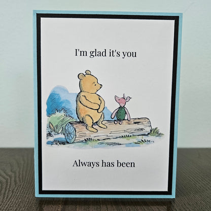 Handmade Winnie the Pooh friendship card featuring a classic watercolor illustration of Pooh and Piglet sitting side by side on a log, accented by a soft sky-blue layered border.
