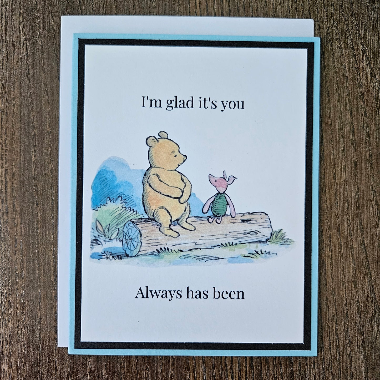 Handmade Winnie the Pooh friendship card featuring a classic watercolor illustration of Pooh and Piglet sitting side by side on a log, accented by a soft sky-blue layered border.