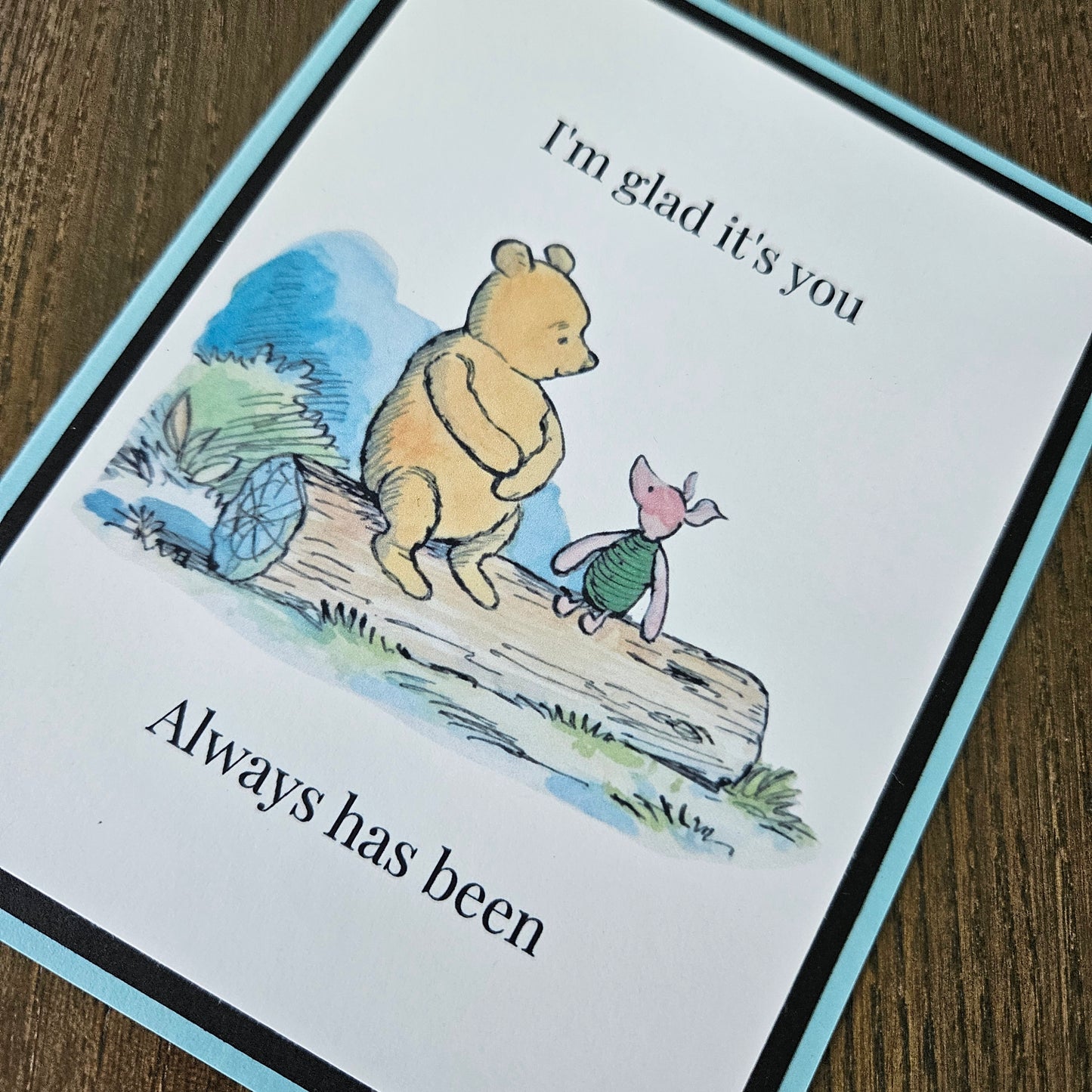 Handmade Winnie the Pooh friendship card featuring a classic watercolor illustration of Pooh and Piglet sitting side by side on a log, accented by a soft sky-blue layered border.