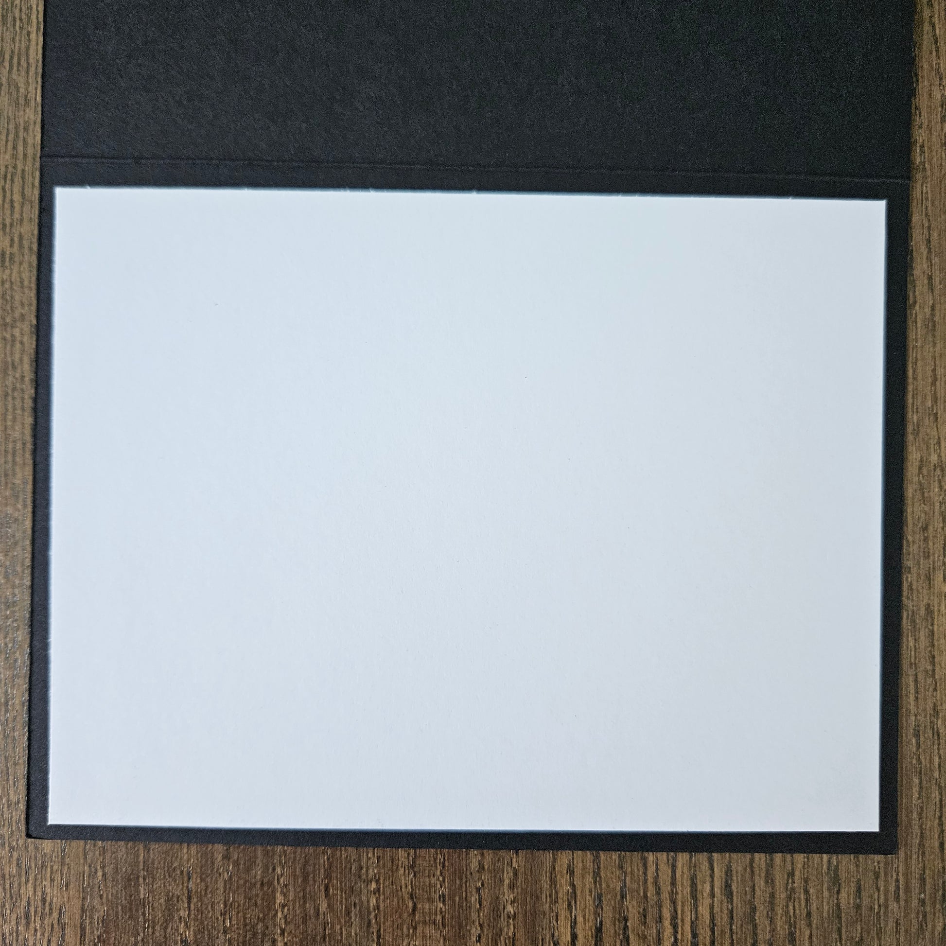 White sheet of paper in a black folder on a wooden surface