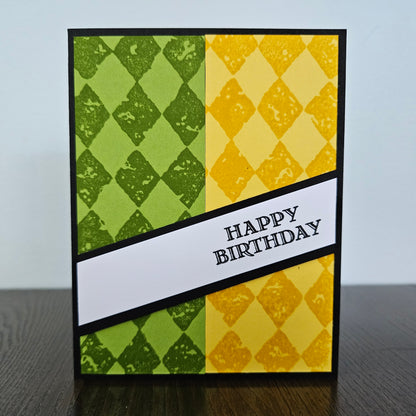 Handmade birthday card for him with green and yellow argyle stamped panels and diagonal banner on black border. Text reads Happy Birthday.