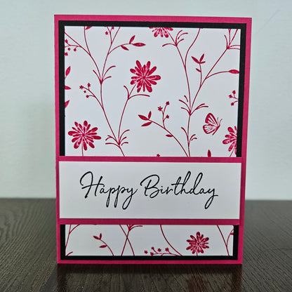 Handmade birthday card for her with pink hand-stamped wildflowers and butterfly design with split banner on black and pink border. Text reads Happy Birthday.