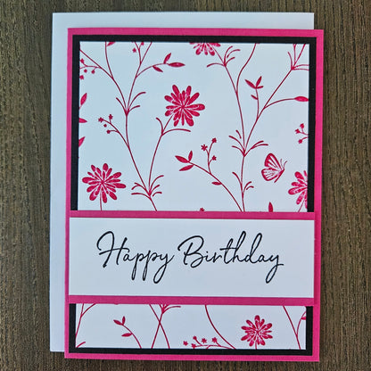 Handmade birthday card for her with pink hand-stamped wildflowers and butterfly design with split banner on black and pink border. Text reads Happy Birthday.