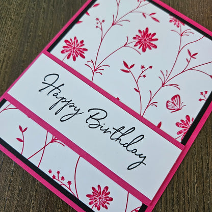 Birthday card with pink floral design and 'Happy Birthday' text on a wooden surface
