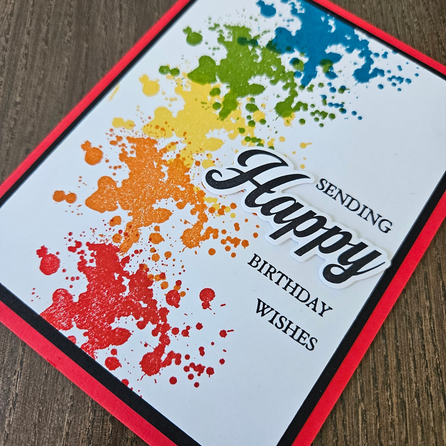 Colorful splatter design birthday card with text on a wooden surface