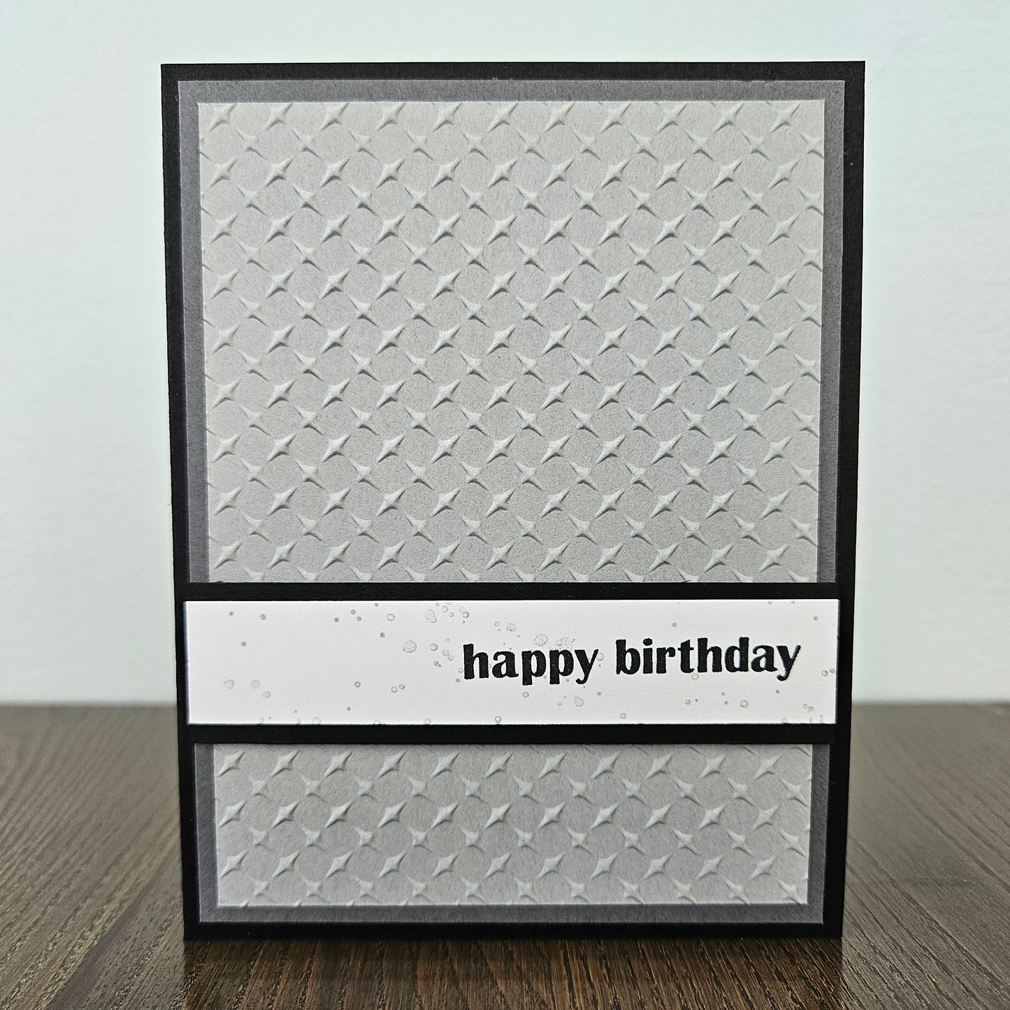 Handmade birthday card with embossed silver grey diamond pattern and bold lowercase happy birthday sentiment banner on black border.