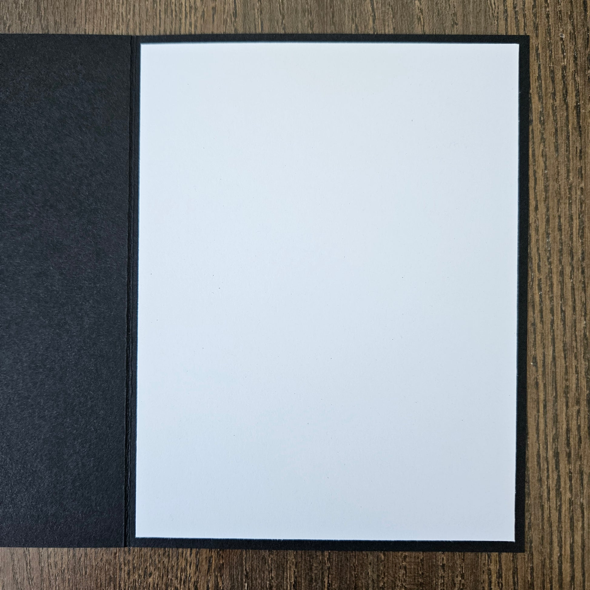 White sheet of paper in a black frame on a wooden surface