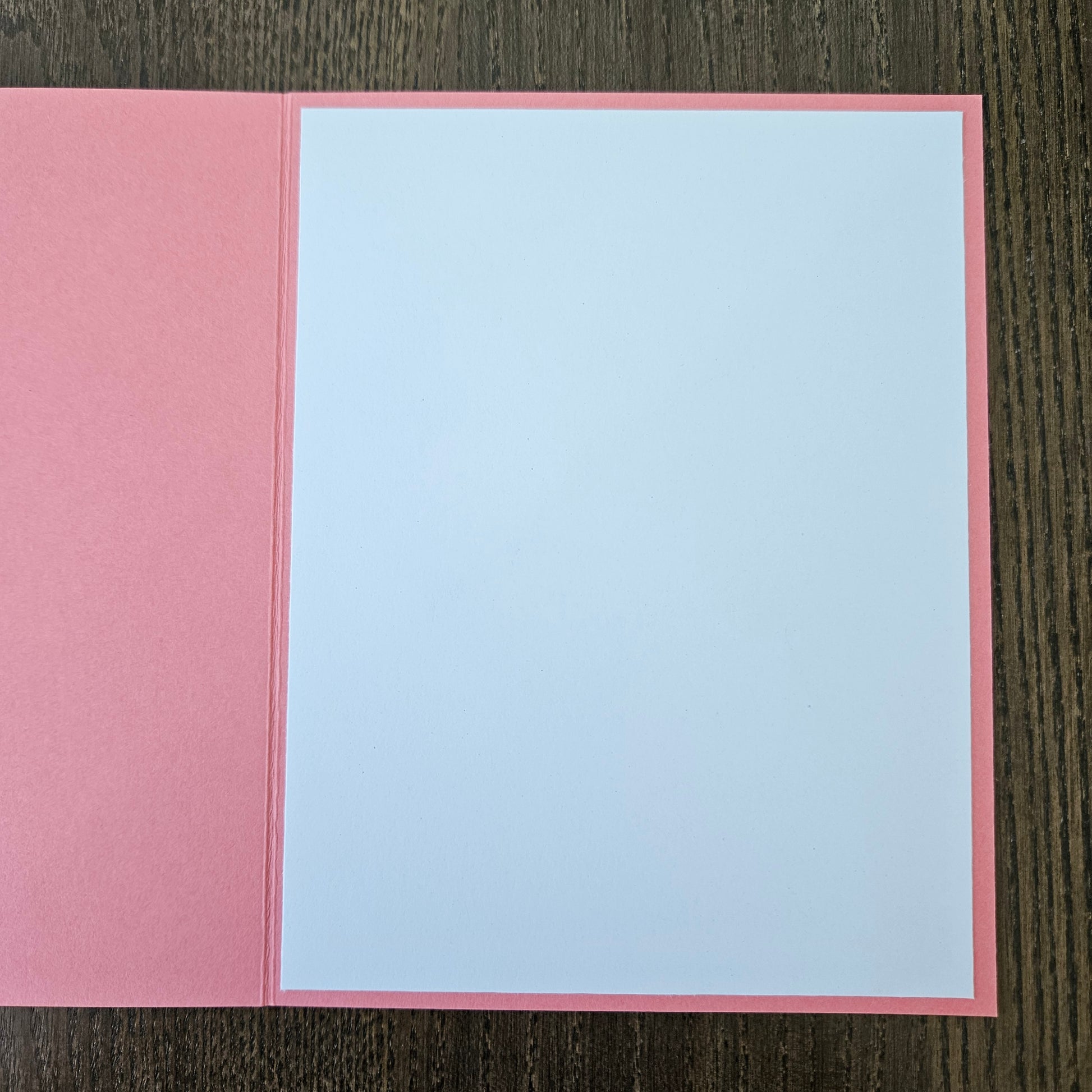 Pink card with a white interior on a wooden surface