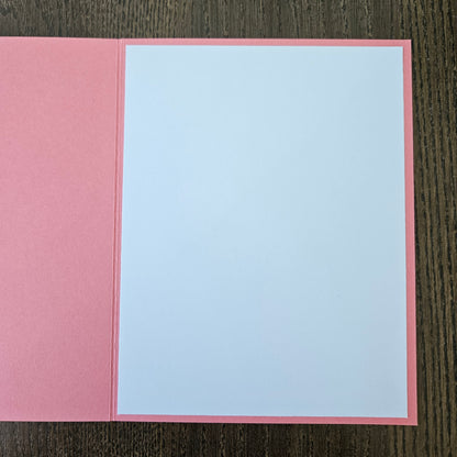 Pink card with a white interior on a wooden surface