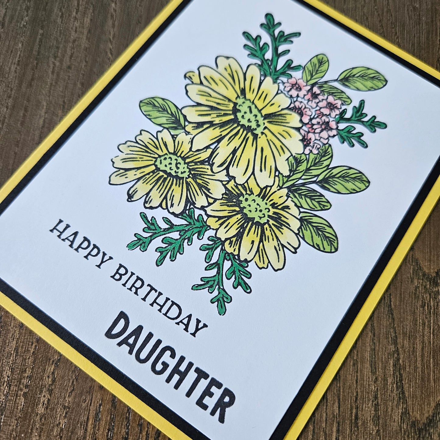 Greeting card with floral design and 'Happy Birthday Daughter' text on a wooden surface