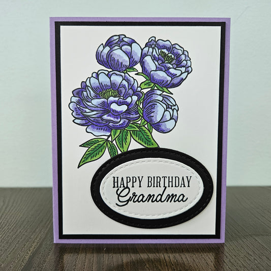 Handmade birthday card for Grandma with hand-colored purple peony bouquet and layered die-cut oval sentiment on white inner panel with black and lavender border. Text reads Happy Birthday Grandma.