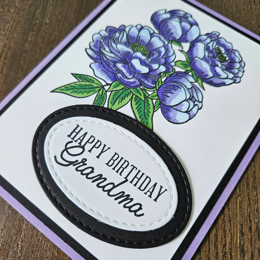 Greeting card with purple flowers and 'Happy Birthday Grandma' text on a wooden surface