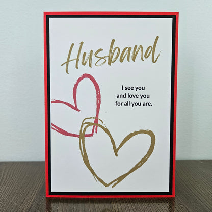 Handmade birthday card for husband from wife front featuring gold brush script text reading Husband and a heartfelt quote, accented by interlocking red and gold hand-drawn hearts, framed by a sharp black inner border and a vibrant red outer card base.