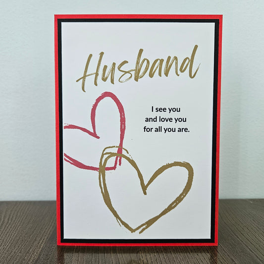 Handmade birthday card for husband from wife front featuring gold brush script text reading Husband and a heartfelt quote, accented by interlocking red and gold hand-drawn hearts, framed by a sharp black inner border and a vibrant red outer card base.