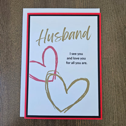Handmade birthday card for husband from wife front featuring gold brush script text reading Husband and a heartfelt quote, accented by interlocking red and gold hand-drawn hearts, framed by a sharp black inner border and a vibrant red outer card base.