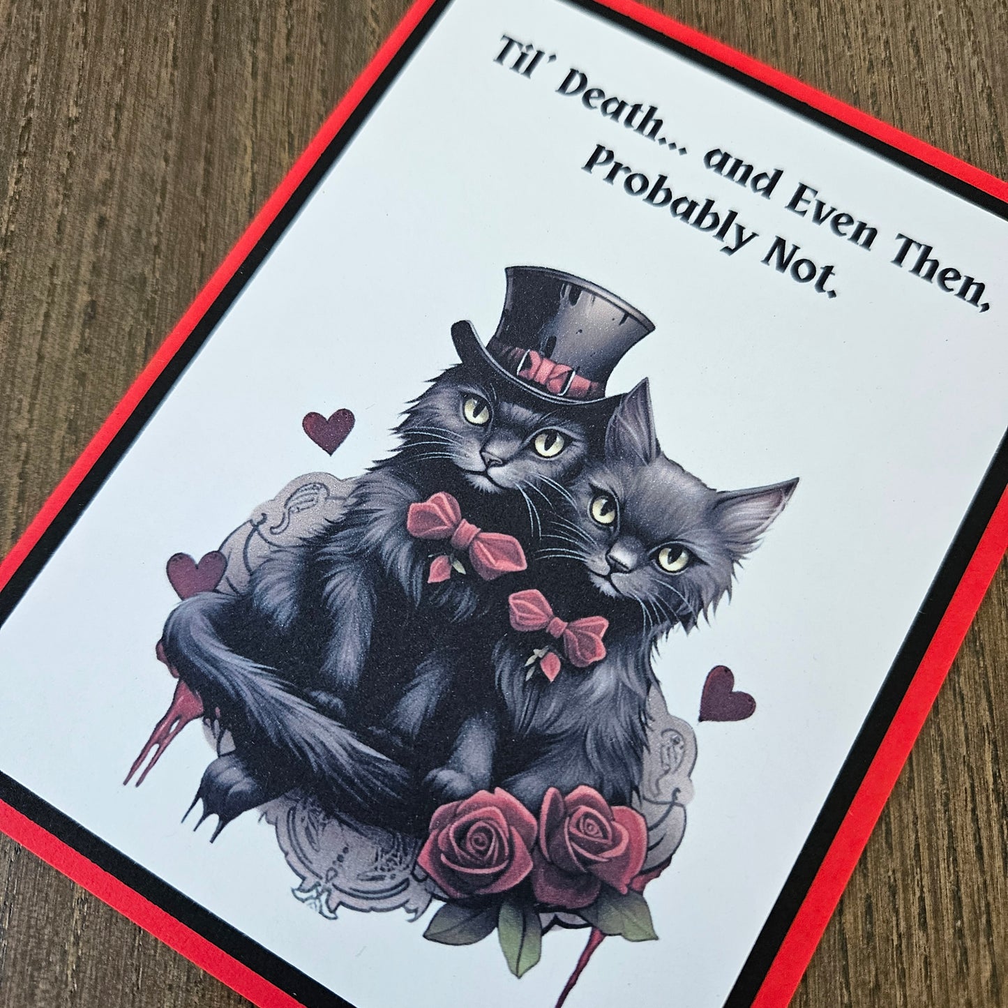 Card with black cat illustration, roses, and text on a wooden surface