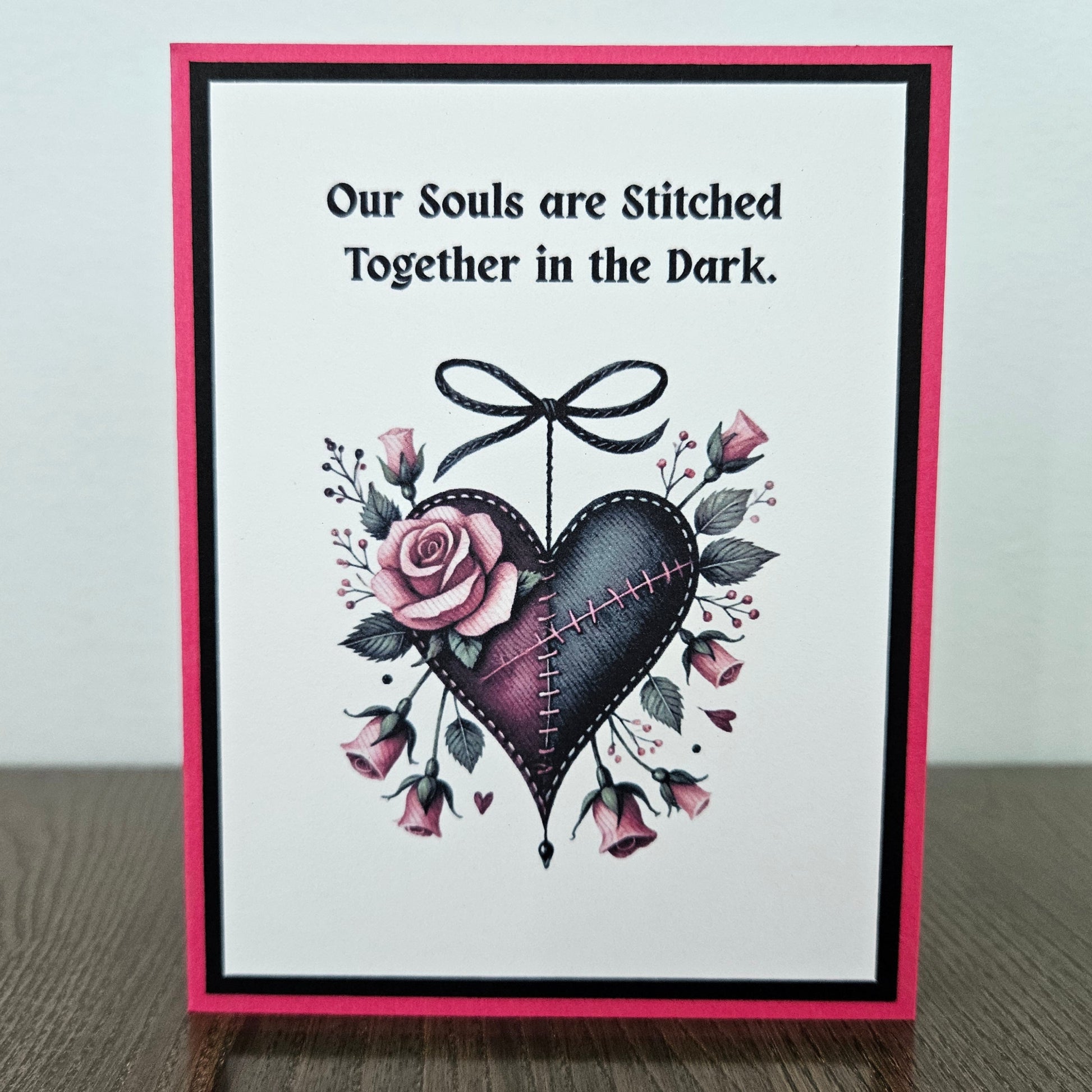 Handmade gothic Valentine card featuring an illustrated purple and black stitched heart with a black bow and pink roses on a hot pink and black layered frame. Text reads Our Souls are Stitched Together in the Dark.
