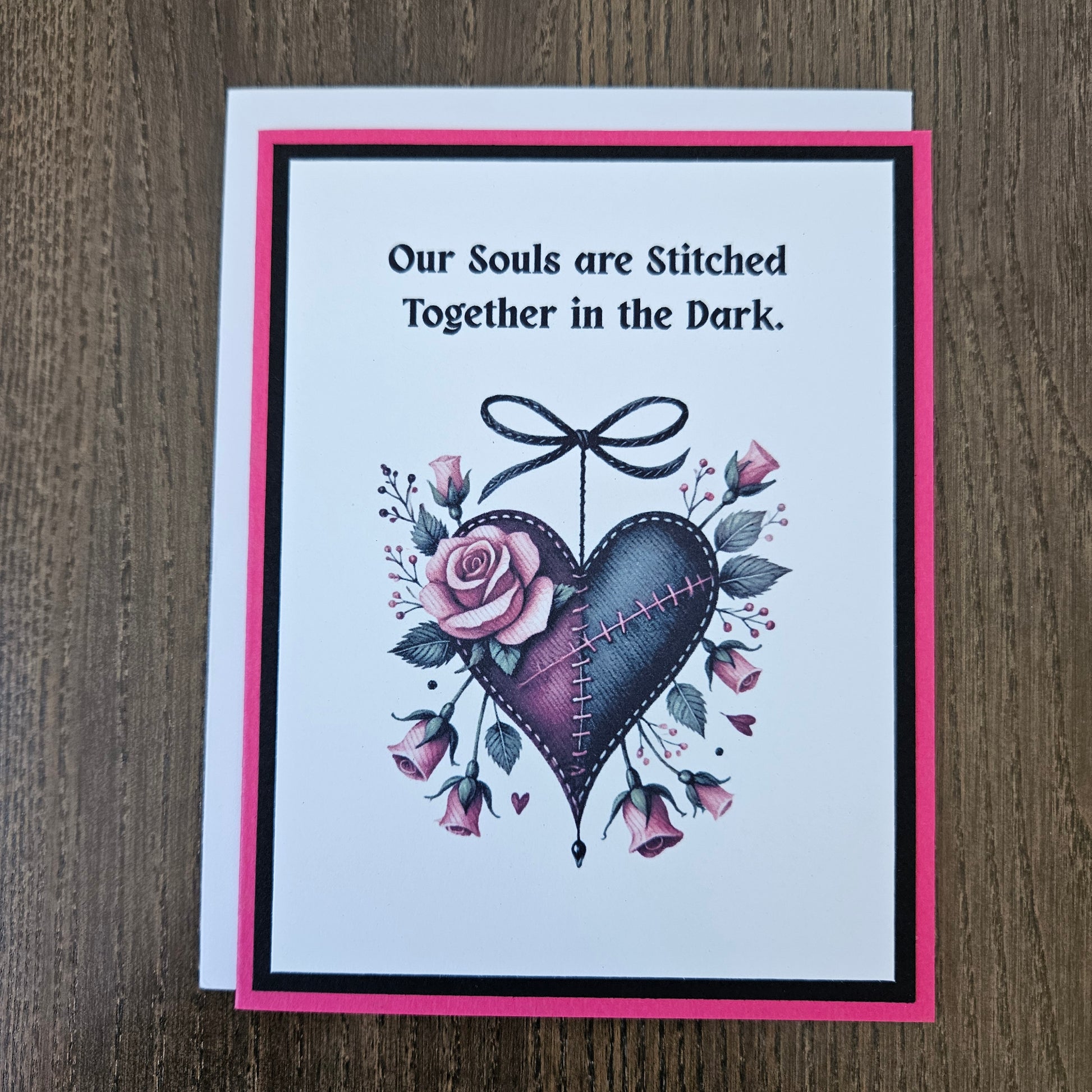 Handmade gothic Valentine card featuring an illustrated purple and black stitched heart with a black bow and pink roses on a hot pink and black layered frame. Text reads Our Souls are Stitched Together in the Dark.