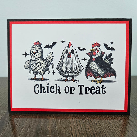 Front of a handmade A2 Halloween card featuring three chickens in mummy, ghost, and vampire costumes below a sentiment block reading Chick or Treat, layered with cardstock framing.