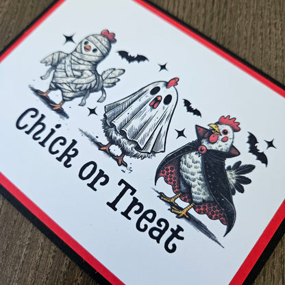 A square printed card or sign with a Halloween-themed illustration showing a chicken dressed as a mummy, a chicken dressed as a ghost, bats, and the words 'Chick or Treat' on a white background with red and black borders.