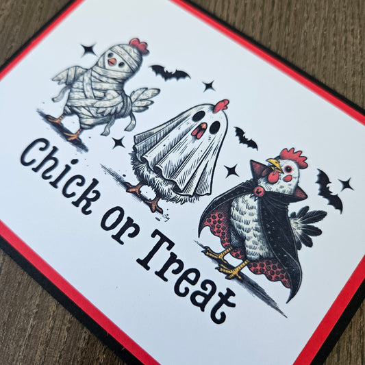 A square printed card or sign with a Halloween-themed illustration showing a chicken dressed as a mummy, a chicken dressed as a ghost, bats, and the words 'Chick or Treat' on a white background with red and black borders.