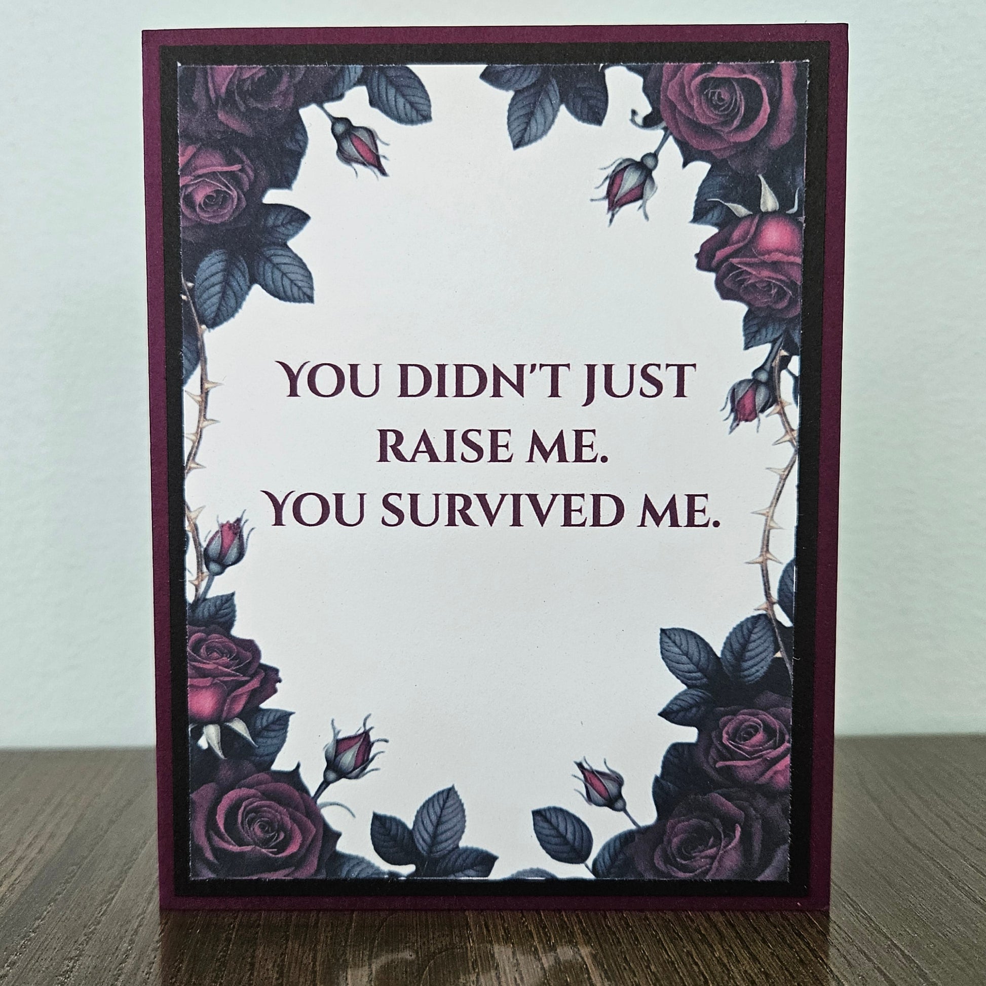 Handmade gothic card for mom featuring a border of dark purple and magenta roses with thorns around text reading You Didn't Just Raise Me. You Survived Me. Inside features a heartfelt message printed on a premium plum cardstock layer.