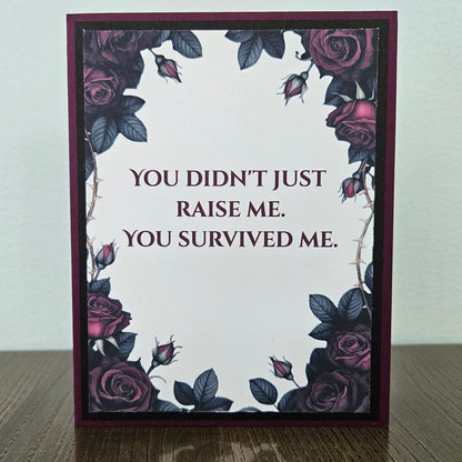 Handmade gothic card for mom featuring a border of dark purple and magenta roses with thorns around text reading You Didn't Just Raise Me. You Survived Me. Inside features a heartfelt message printed on a premium plum cardstock layer.