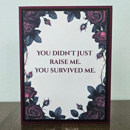 Handmade gothic card for mom featuring a border of dark purple and magenta roses with thorns around text reading You Didn't Just Raise Me. You Survived Me. Inside features a heartfelt message printed on a premium plum cardstock layer.