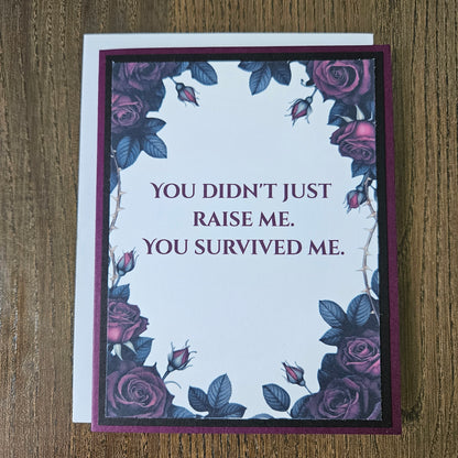 Handmade gothic card for mom featuring a border of dark purple and magenta roses with thorns around text reading You Didn't Just Raise Me. You Survived Me. Inside features a heartfelt message printed on a premium plum cardstock layer.