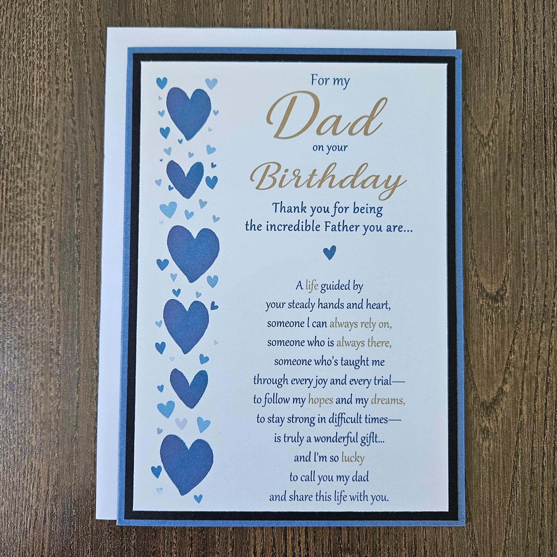 Front of a handmade 5x7 birthday card for Dad featuring a vertical border of stenciled blue hearts on the left and a gold and blue printed poem on a white panel, layered with a black border and a blue card base.