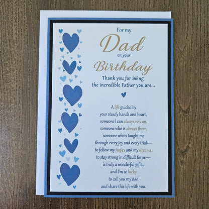 Front of a handmade 5x7 birthday card for Dad featuring a vertical border of stenciled blue hearts on the left and a gold and blue printed poem on a white panel, layered with a black border and a blue card base.