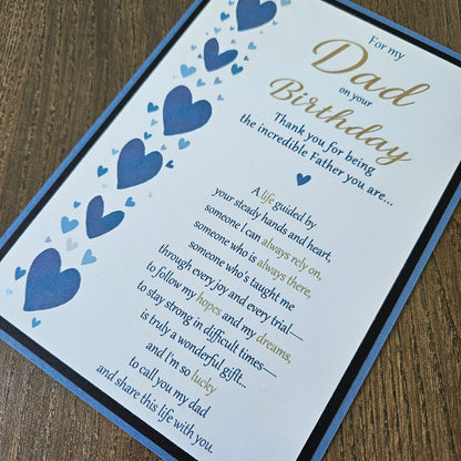 Front of a handmade 5x7 birthday card for Dad featuring a vertical border of stenciled blue hearts on the left and a gold and blue printed poem on a white panel, layered with a black border and a blue card base.