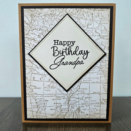 a handmade A2 birthday card featuring a sepia-toned vintage world map background pattern and a raised cream-colored stitched diamond layer that reads Happy Birthday Grandpa, finished with a sharp black mat and kraft brown cardstock frame.