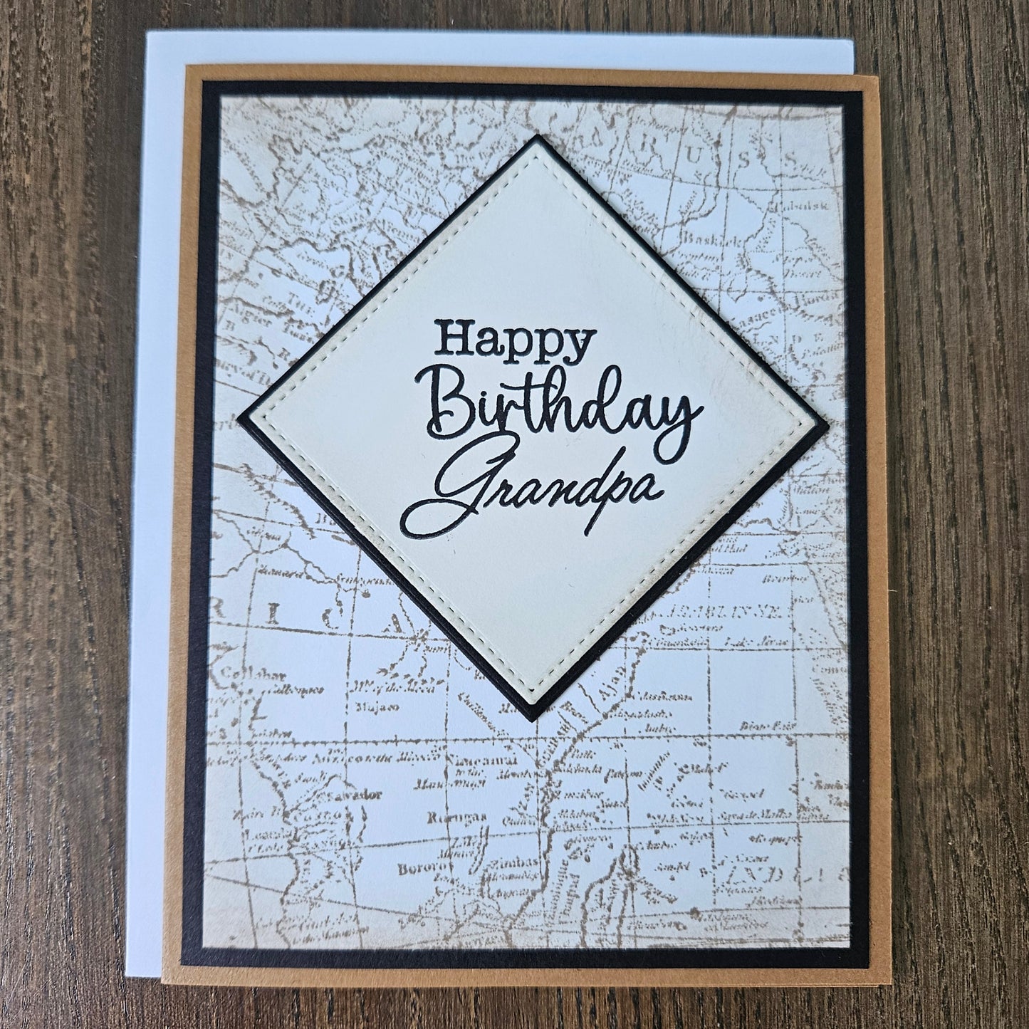 a handmade A2 birthday card featuring a sepia-toned vintage world map background pattern and a raised cream-colored stitched diamond layer that reads Happy Birthday Grandpa, finished with a sharp black mat and kraft brown cardstock frame.