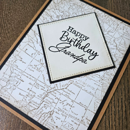 a handmade A2 birthday card featuring a sepia-toned vintage world map background pattern and a raised cream-colored stitched diamond layer that reads Happy Birthday Grandpa, finished with a sharp black mat and kraft brown cardstock frame.