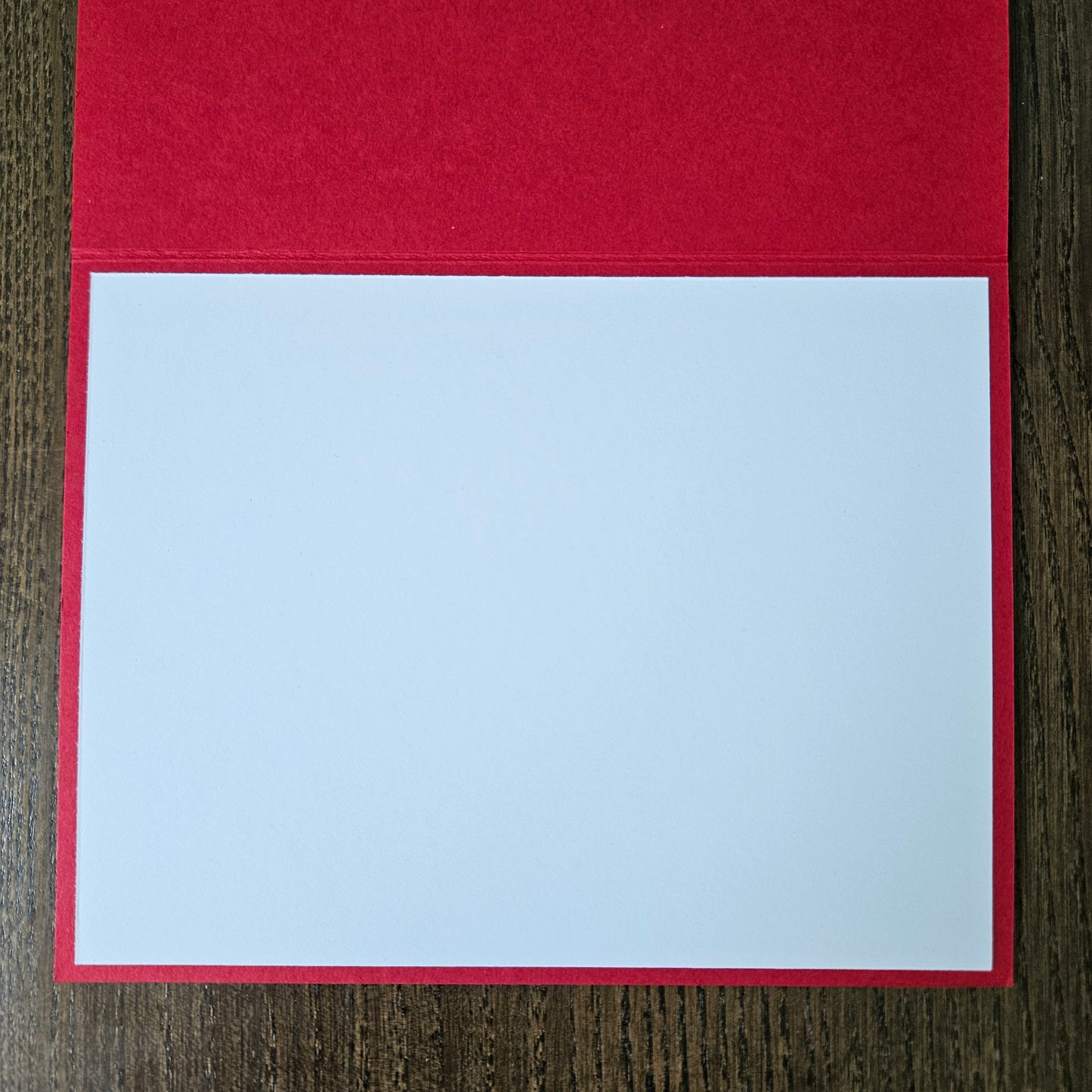 A blank white writing pad sheet with a red border, displayed open on a dark wood background.